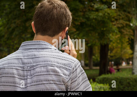 Back view of casual man walking in park of Madrid and having phone conversation. Stock Photo