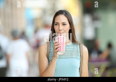 Front view portrait of a woman walking and drinking a takeaway refreshment in the street Stock Photo