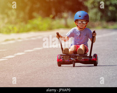 Happy boy standing on hoverboard or gyroscooter with kart accessory kit outdoor. New modern technologies Stock Photo