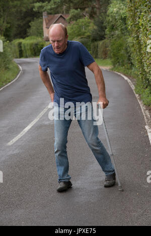 Elderly disabled man with back pain using a walking stick Stock Photo