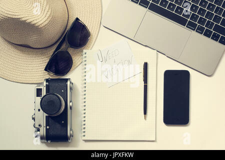 Thoughts about vacation workplace. Weekend mood. Blogger, writer or freelancer desk with laptop, open notebook, phone, pen, hat, old camera, glasses Stock Photo