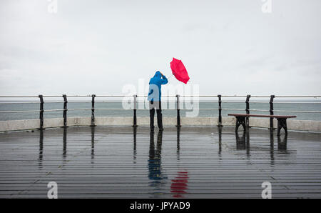 Saltburn by the sea, North Yorkshire, England, UK. 3rd Aug, 2017. UK Weather: A wet and windy start to the day at Saltburn on the North Yorkshire coast, with the sun finally breaking through late morning. PICTURED: A man struggles with his umbrella at the end of Saltburn`s Victorian pier early on Thursday morning. Credit: ALAN DAWSON/Alamy Live News Stock Photo
