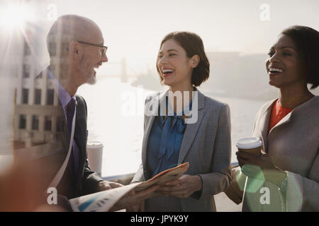 Silhouetted business people laughing, drinking coffee and reading newspaper on sunny urban bridge Stock Photo