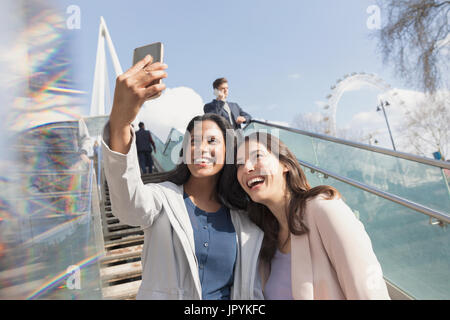 Enthusiastic, smiling women friends taking selfie with camera phone on sunny, urban stairs, London, UK Stock Photo
