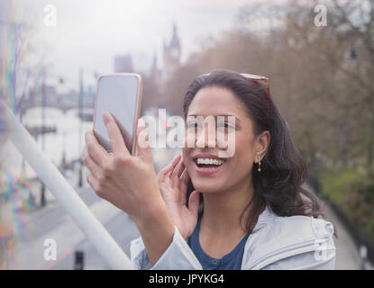 Smiling, confident woman taking selfie with camera phone on urban bridge Stock Photo