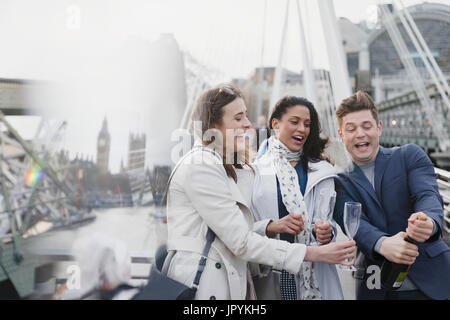 Friends popping champagne, celebrating on urban bridge, London, UK Stock Photo