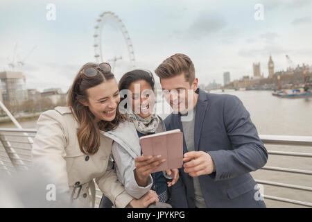Friend tourists using digital tablet on bridge over Thames River, London, UK Stock Photo