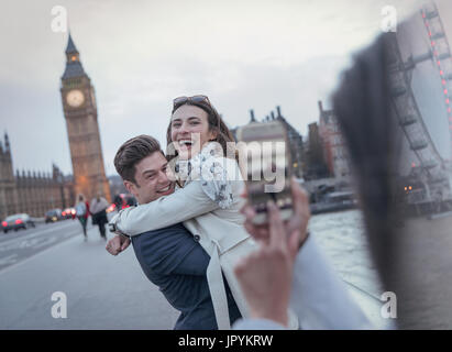 Playful couple tourists being photographed on bridge near Big Ben, London, UK Stock Photo
