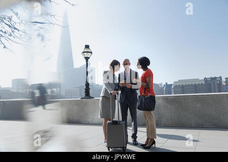 Business people with suitcase talking, using cell phone in sunny urban park, London, UK Stock Photo