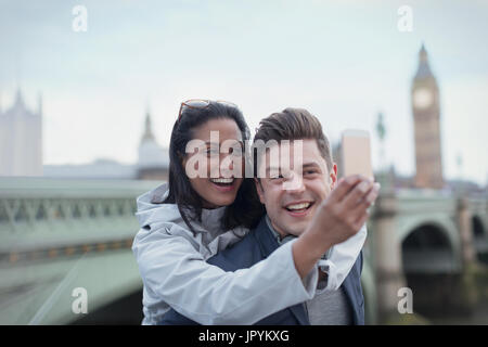 Playful, affectionate couple tourists taking selfie with camera phone in front of Westminster Bridge, London, UK Stock Photo