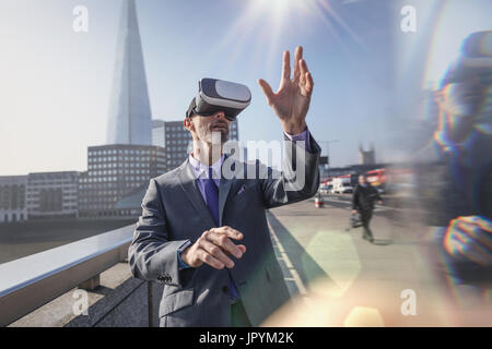 Businessman using virtual reality simulator glasses on sunny urban bridge, London, UK Stock Photo