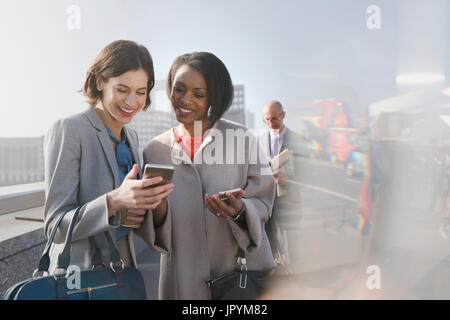 Smiling businesswomen using cell phone on sunny urban bridge Stock Photo