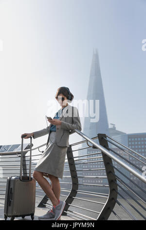 Businesswoman with suitcase listening to music with smart phone and headphones, London, UK Stock Photo