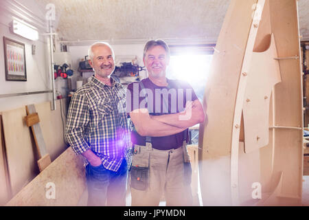 Portrait smiling male carpenters making wood boat in workshop Stock Photo