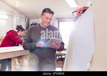 Male carpenter using digital tablet next to wood boat in workshop Stock Photo