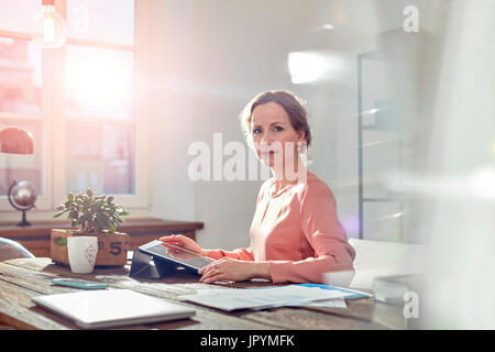 Portrait confident businesswoman using digital tablet at desk in office Stock Photo