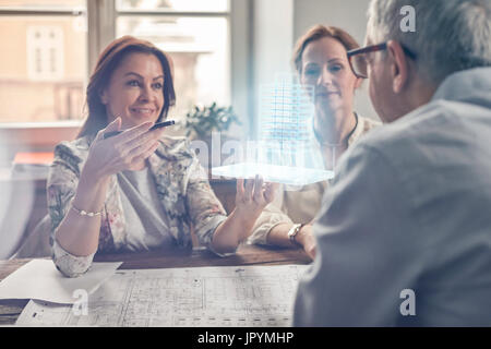 Architects with blueprints examining plastic model in office meeting Stock Photo
