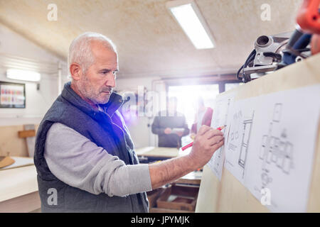Senior male carpenter editing plans in workshop Stock Photo