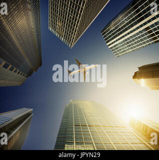 Airplane flying in blue sky over highrise buildings, travel concept Stock Photo