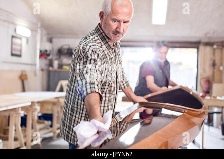 Senior man finishing, wiping wood kayak in workshop Stock Photo