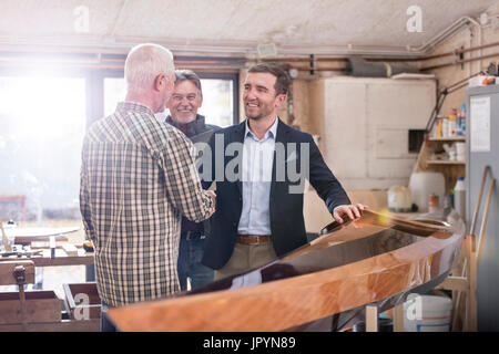 Male carpenters handshaking with satisfied customer next to wood kayak in workshop Stock Photo