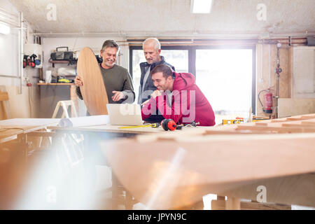 Male carpenters using laptop near wood boat in workshop Stock Photo