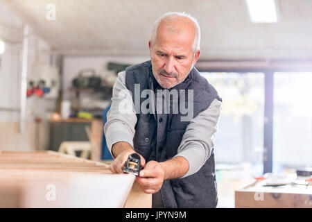 Focused senior male carpenter using jack plane on wood boat in workshop Stock Photo