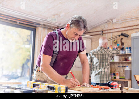 Male carpenter measuring and marking wood plank on workbench in workshop Stock Photo