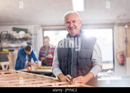 Portrait smiling male carpenter working on wood boat in workshop Stock Photo