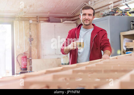 Portrait confident male carpenter drinking tea at wood boat in workshop Stock Photo