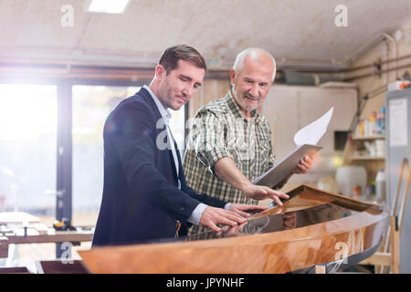 Male carpenter and customer examining wood kayak in workshop Stock Photo