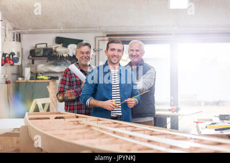 Portrait smiling male carpenters working at wood boat in workshop Stock Photo