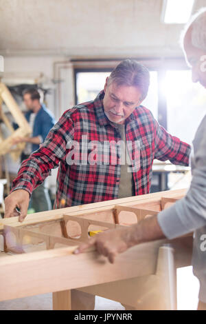 Male carpenters examining wood boat in workshop Stock Photo