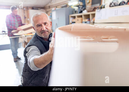 Male carpenter examining, touching wood boat in workshop Stock Photo