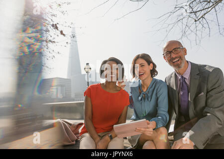 Portrait smiling business people using digital tablet in sunny urban park Stock Photo