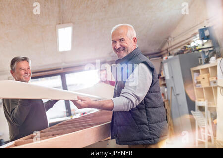 Portrait smiling senior male carpenter lifting wood boat in workshop Stock Photo