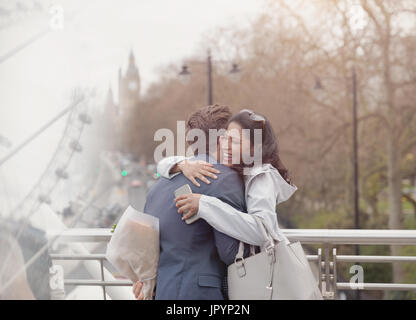 Smiling couple hugging, boyfriend surprising girlfriend with flowers on urban bridge, London, UK Stock Photo