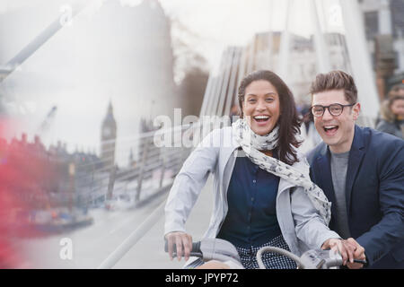 Portrait playful couple bike riding on urban city road, London, UK Stock Photo