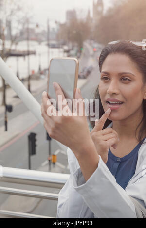 Woman checking makeup with camera phone on urban bridge, London, UK Stock Photo