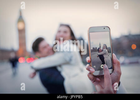 Personal perspective, playful couple hugging and being photographed with camera phone near Big Ben, London, UK Stock Photo