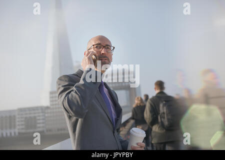 Serious businessman drinking coffee and talking on cell phone, London, UK Stock Photo