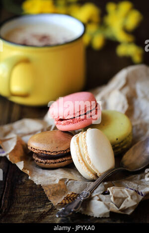 Delicious French macaroons on sack kraft paper with cappuccino coffee at the background on dar rustic wooden table Stock Photo