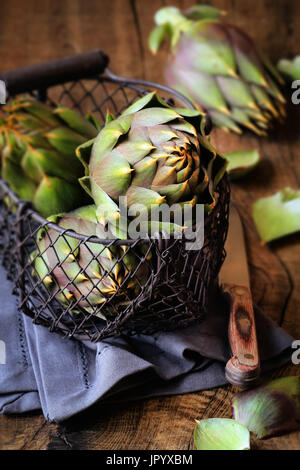 Sardinian thorny artichokes in a wire basket on dark rustic wooden background Stock Photo