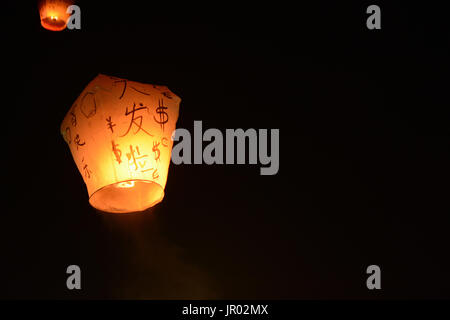 Sky lantern floating into the night sky at the festival in Pingxi, the Chinese text is a wish for money in the New Year Stock Photo