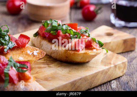 Tomato and basil bruschetta with toasted garlic bread, traditional Italian appetizer on rustic wooden cutting board Stock Photo