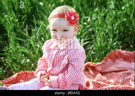 Little girl is sitting on a blanket in the summer field Stock Photo