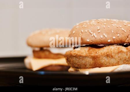 Two tasty and fresh fish burgers on black plate in kitchen. Fast food concept. Stock Photo