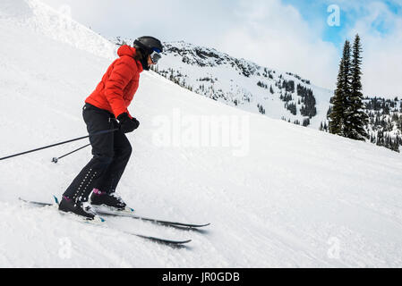 A Downhill Skier In A Red Coat Skiing On The Snow Covered Rocky Mountains; Whistler, British Columbia, Canada Stock Photo