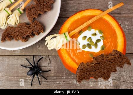 Halloween pumpkin soup with witch's broom and bat bread snacks on a rustic wooden background Stock Photo