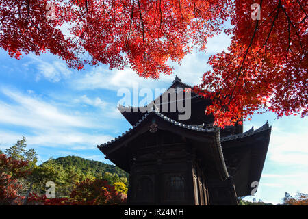 Bright red maple leaves contrast with an ancient temple in Kyoto, Japan Stock Photo